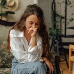 Woman in a white shirt sitting thoughtfully on a vintage sofa indoors.