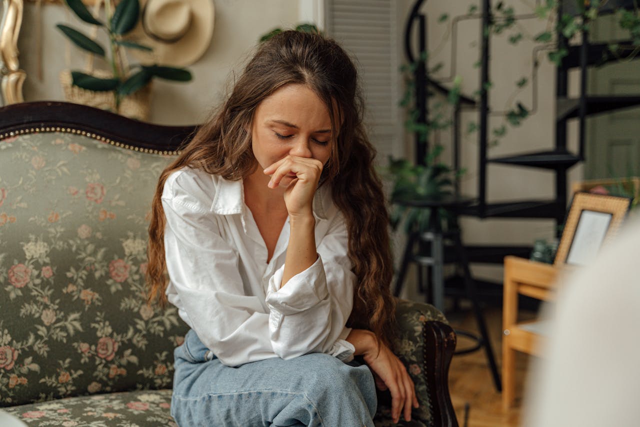 Le Burn-Out : plus qu'un simple coup de fatigue, un signal d'alarme Woman in a white shirt sitting thoughtfully on a vintage sofa indoors.